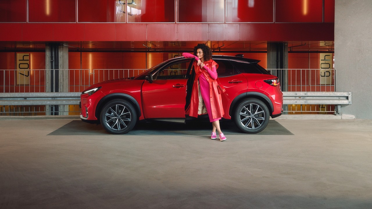 A person leaning against a red Lexus LBX